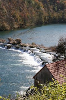 Picturesque waterfall and water mill in a forest setting during fall.